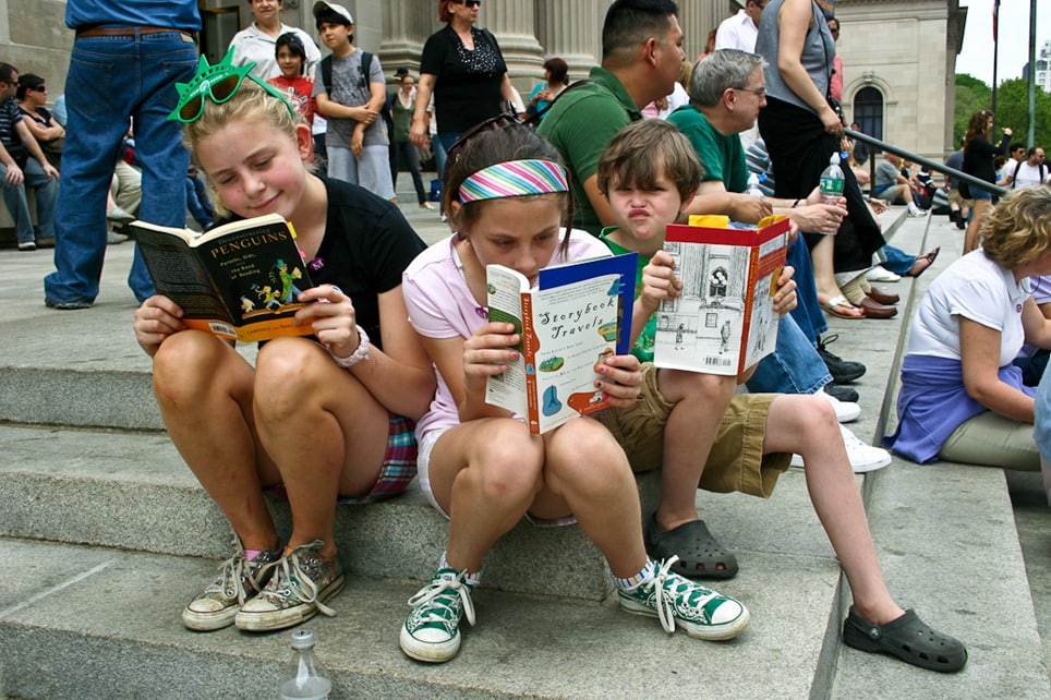 Kids reading about storybook travel on the Met steps in New York City